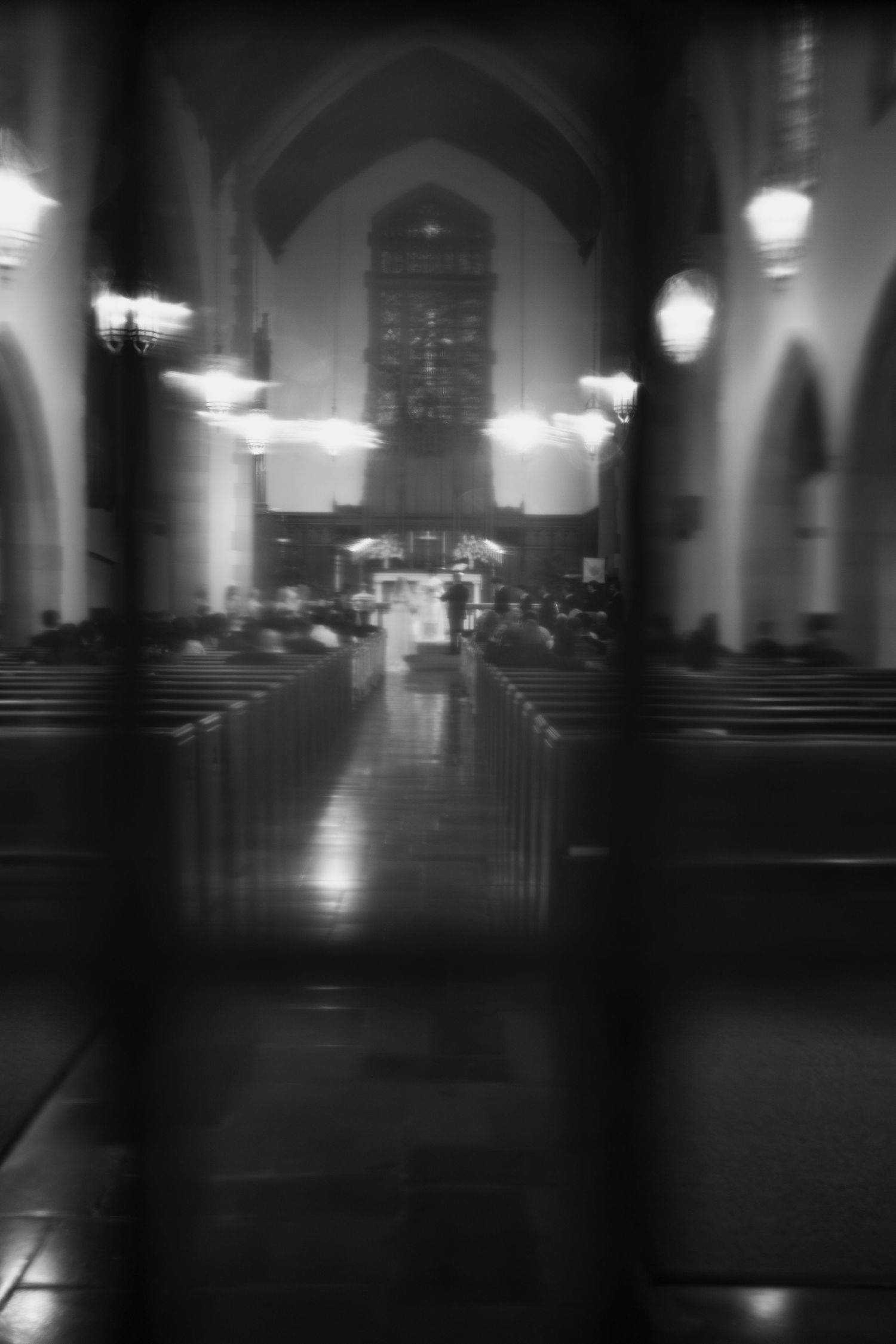 Black and white photo of a church interior with pews, arched ceilings, and altar illuminated by chandeliers.