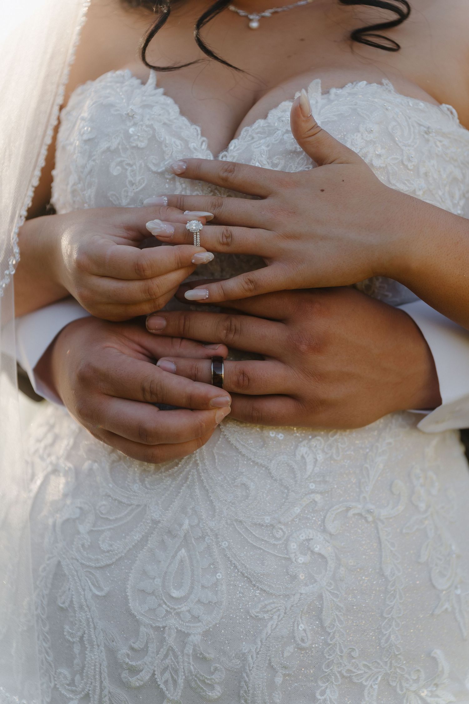 Bride and groom holding hands showing wedding rings, bride wearing lace gown with diamond engagement ring.
