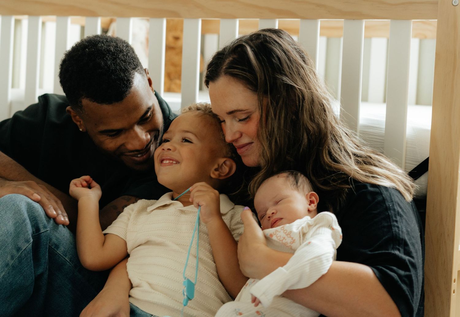 Loving interracial family with parents and two young children, including a newborn baby, sharing a tender moment together.