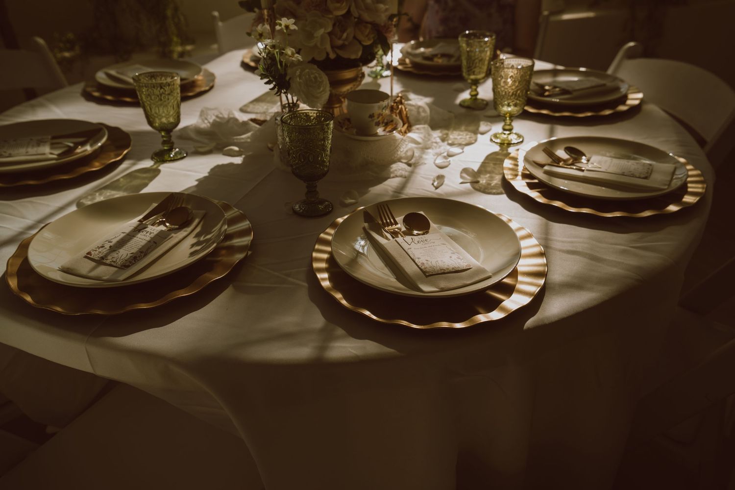 Elegant wedding reception table set with gold charger plates, silverware, and glowing candlelight centerpieces.