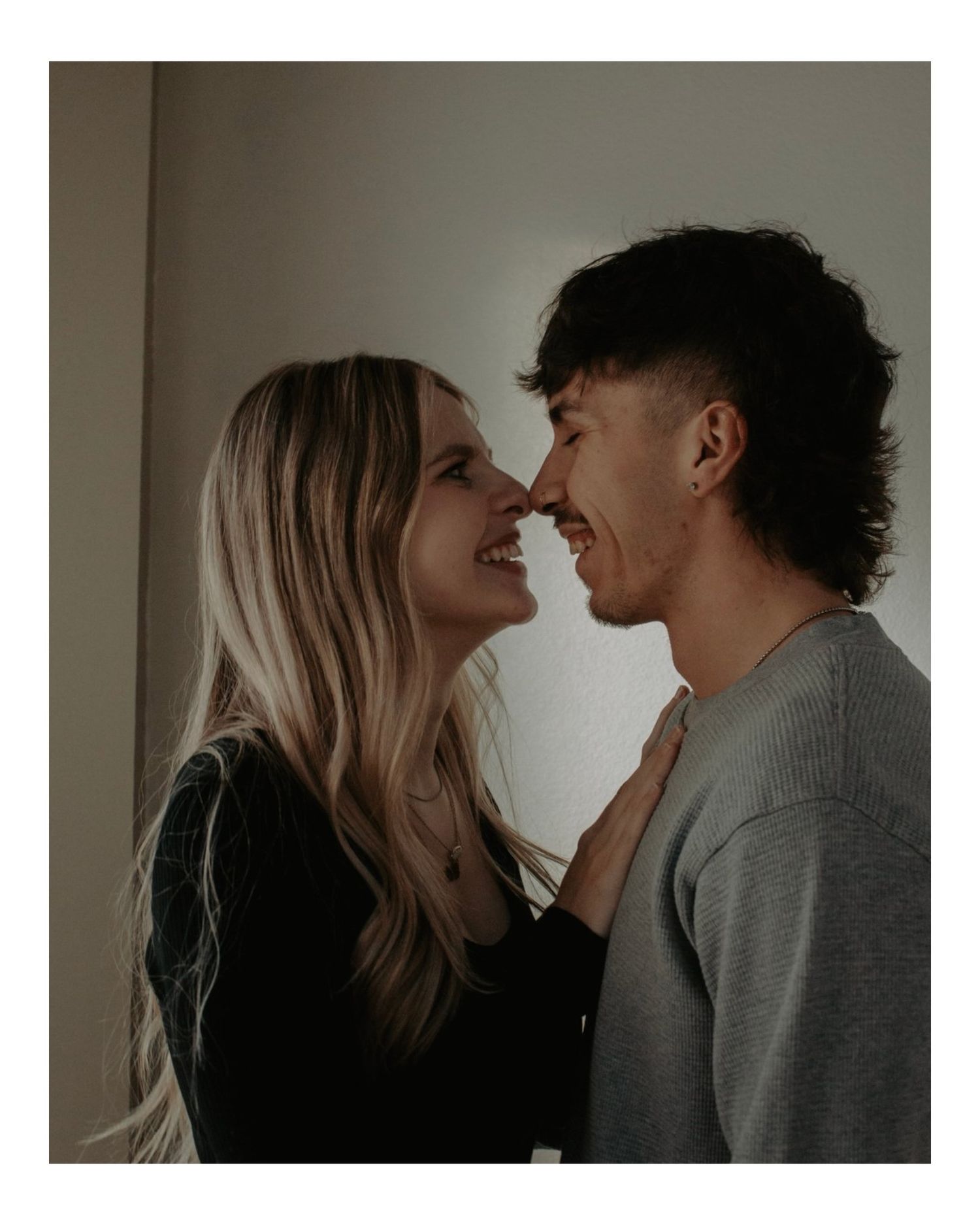 Young couple smiling nose-to-nose in a cozy indoor engagement portrait with soft lighting.