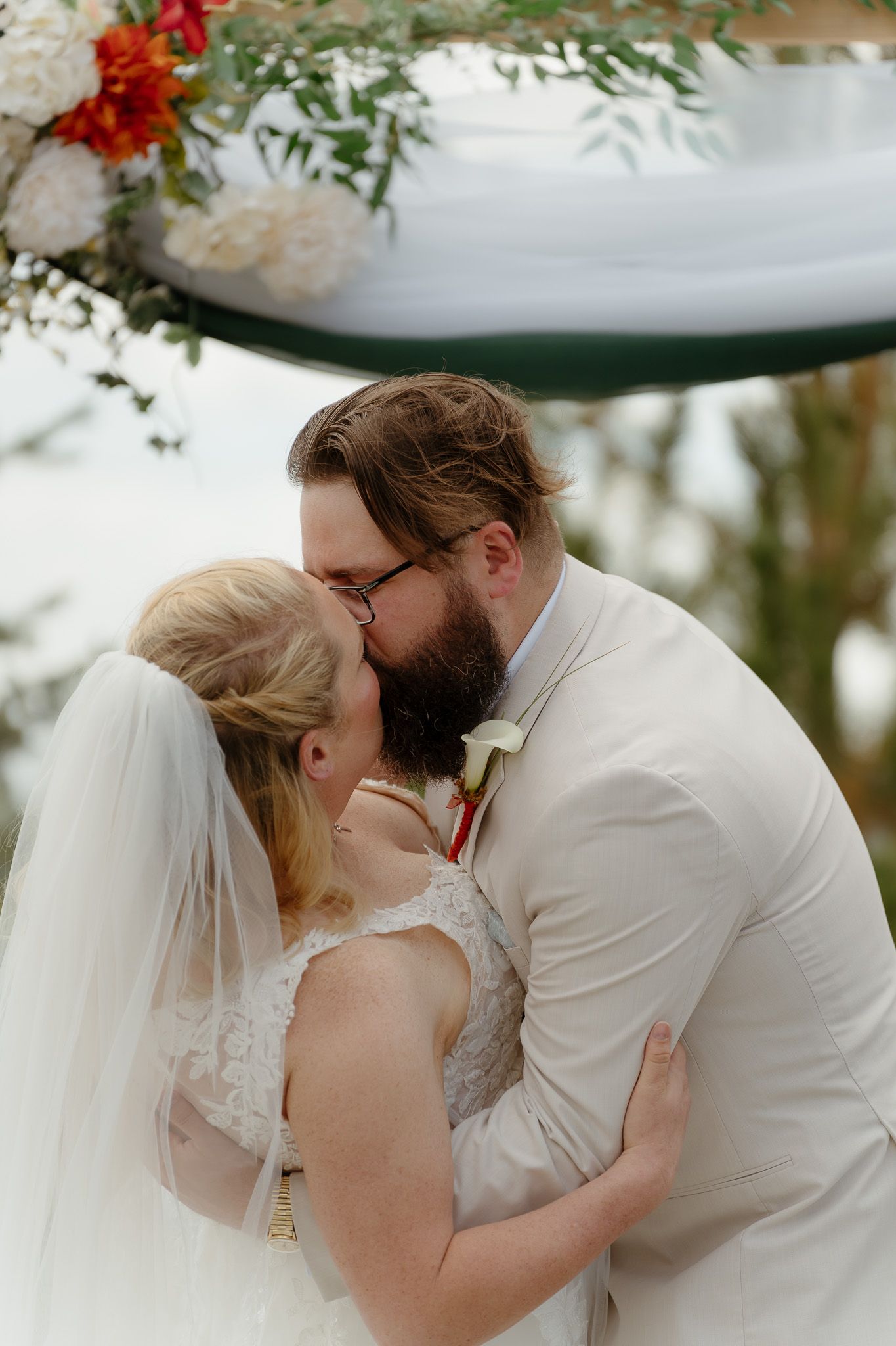 Bride and groom share their first kiss under a floral arch at an outdoor wedding ceremony.