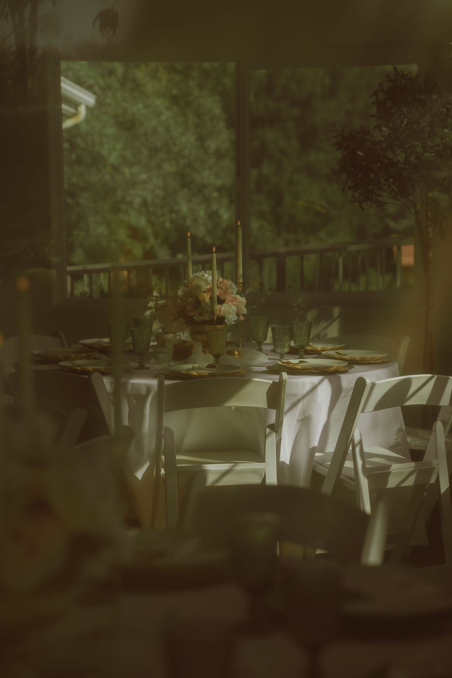 Elegant outdoor wedding reception table with white chairs, floral centerpiece, candles, and gold chargers on a covered patio.
