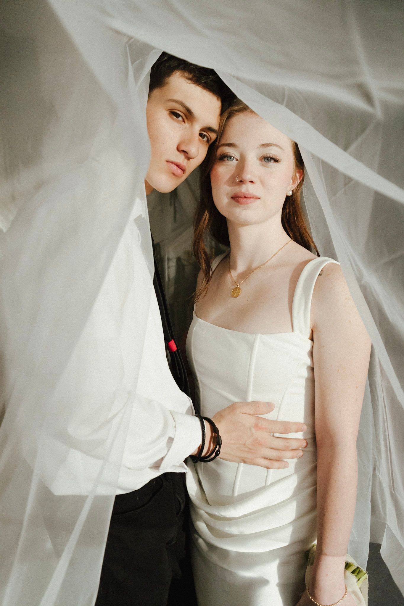 Elegant couple poses under a flowing white veil in a romantic indoor wedding portrait.
