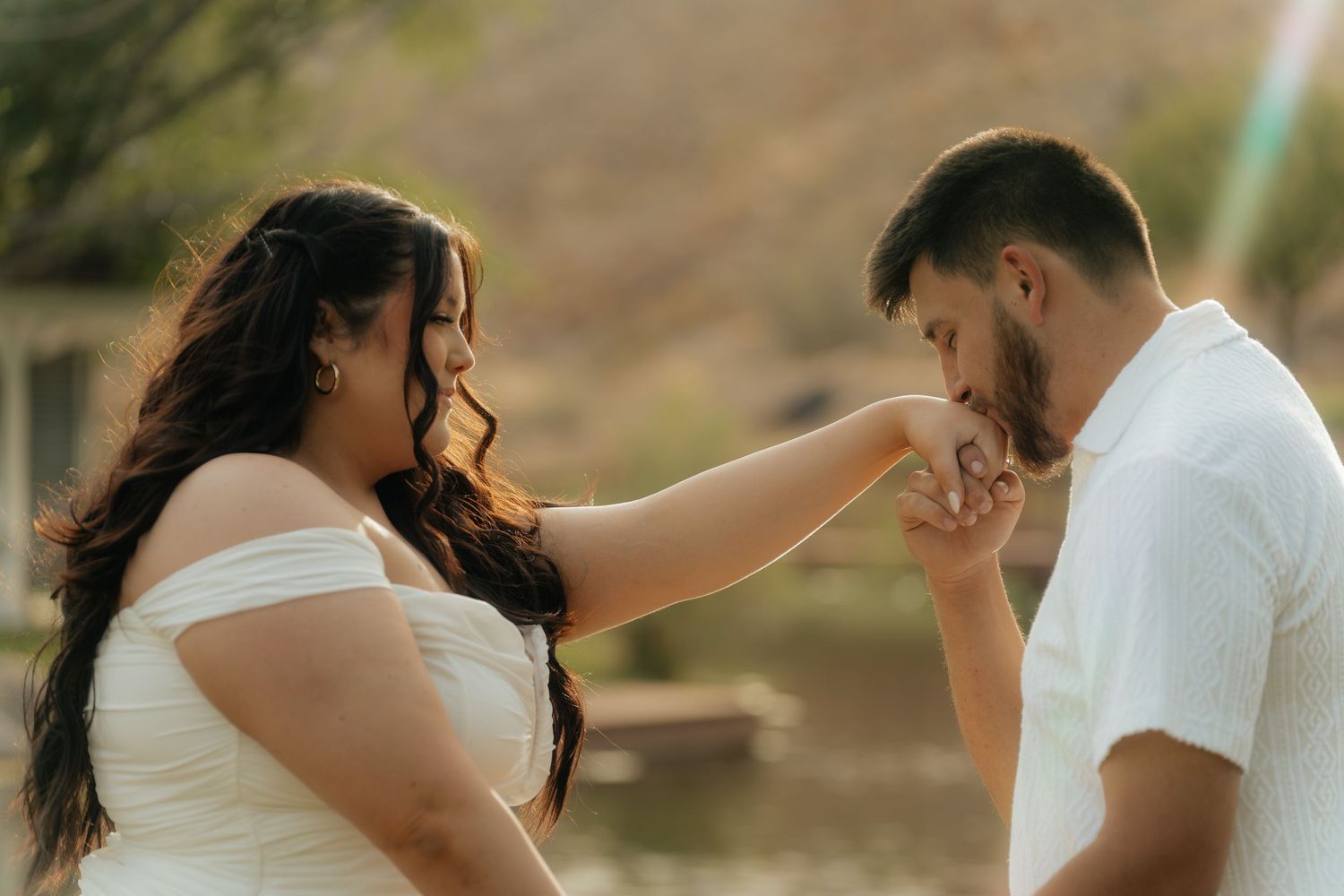 A man in white shirt kisses a woman's hand during a romantic outdoor engagement photo session.