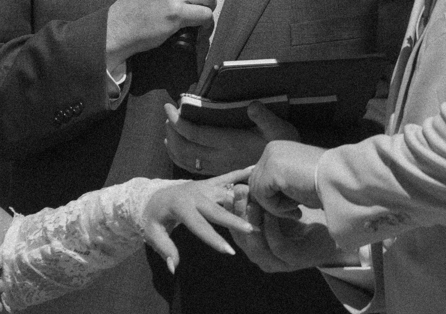 Black and white photo of a groom placing a wedding ring on the bride's finger during a marriage ceremony.