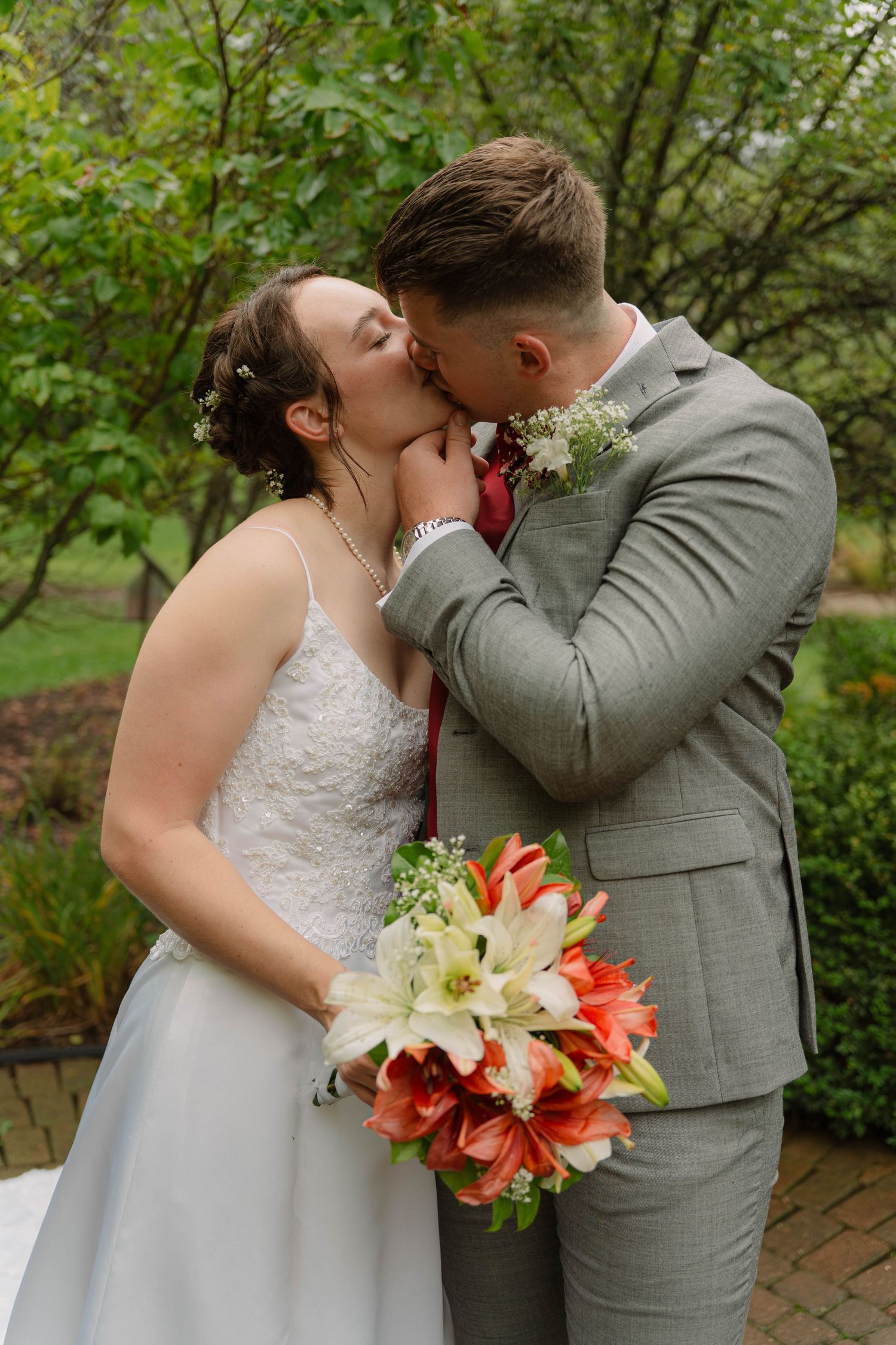 Married couple sharing a kiss at Pamperin Park in Green Bay, Wisconsin wearing wedding dress and grey tuxedo holding pink and white flowers