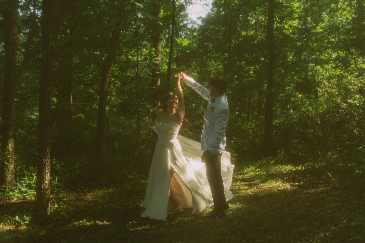 Married couple twirling in green grass with tall pine trees wearing white wedding dress and white tuxedo smiling in Lake Geneva, Wisconsin