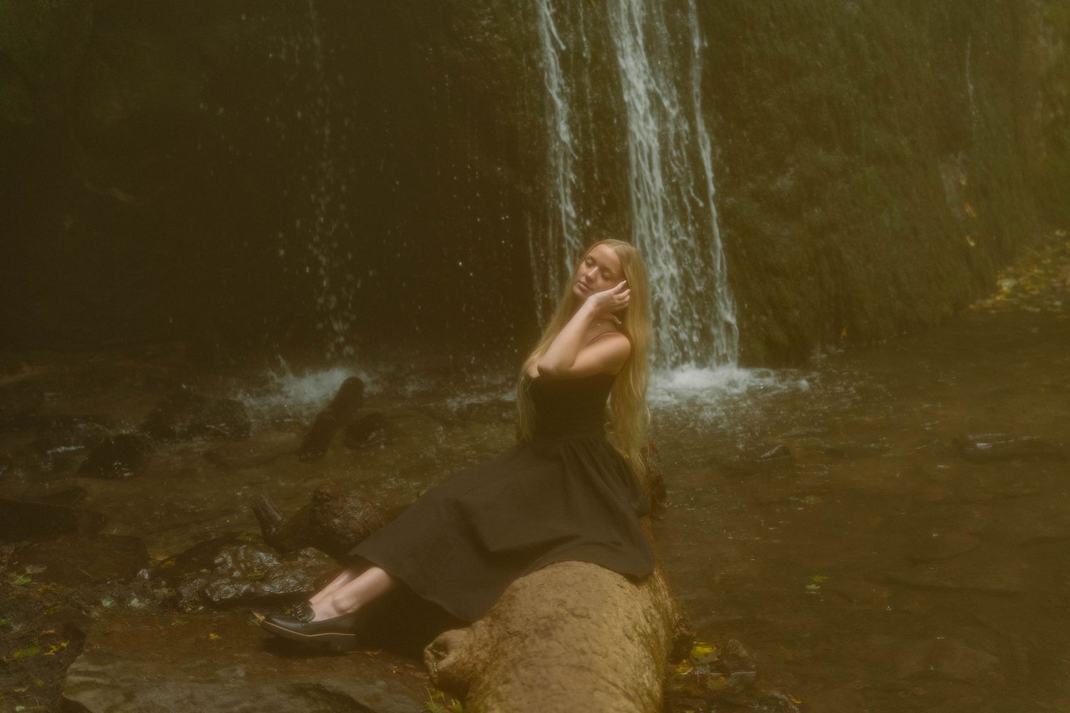 alone girl wearing black dress sitting on tree limb in front of waterfall in Madison, Wisconsin