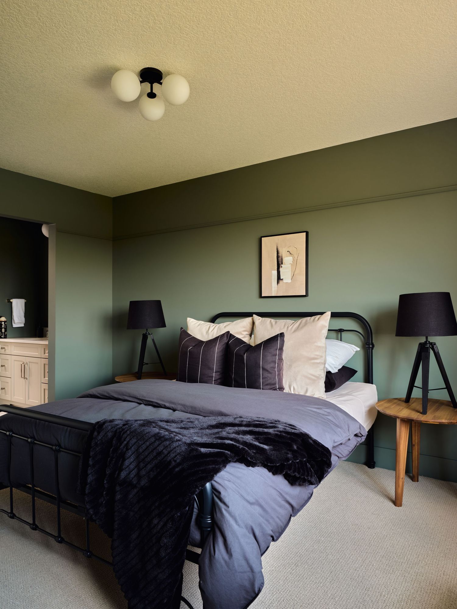 Dark green bedroom with black metal bed frame, gray bedding, tripod lamps, and a globe ceiling light fixture.