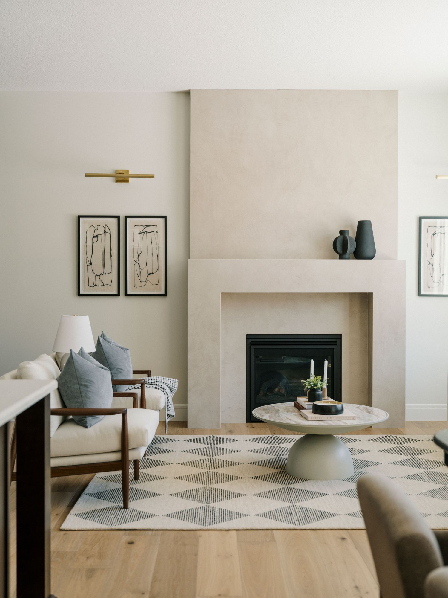 Bright living room featuring plaster fireplace, geometric rug, round coffee table, and neutral furnishings.