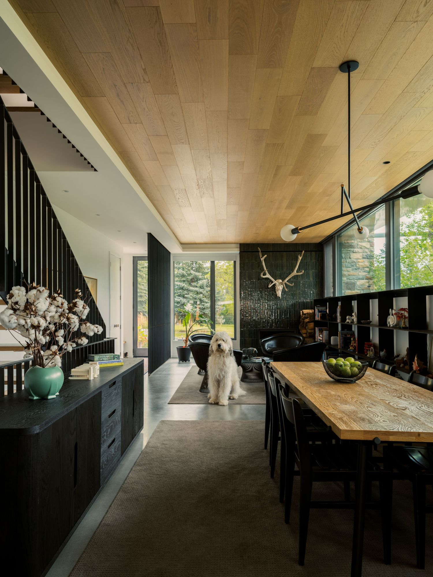 Dark modern dining room with wood ceiling, black cabinetry, butcher block table, and white dog.