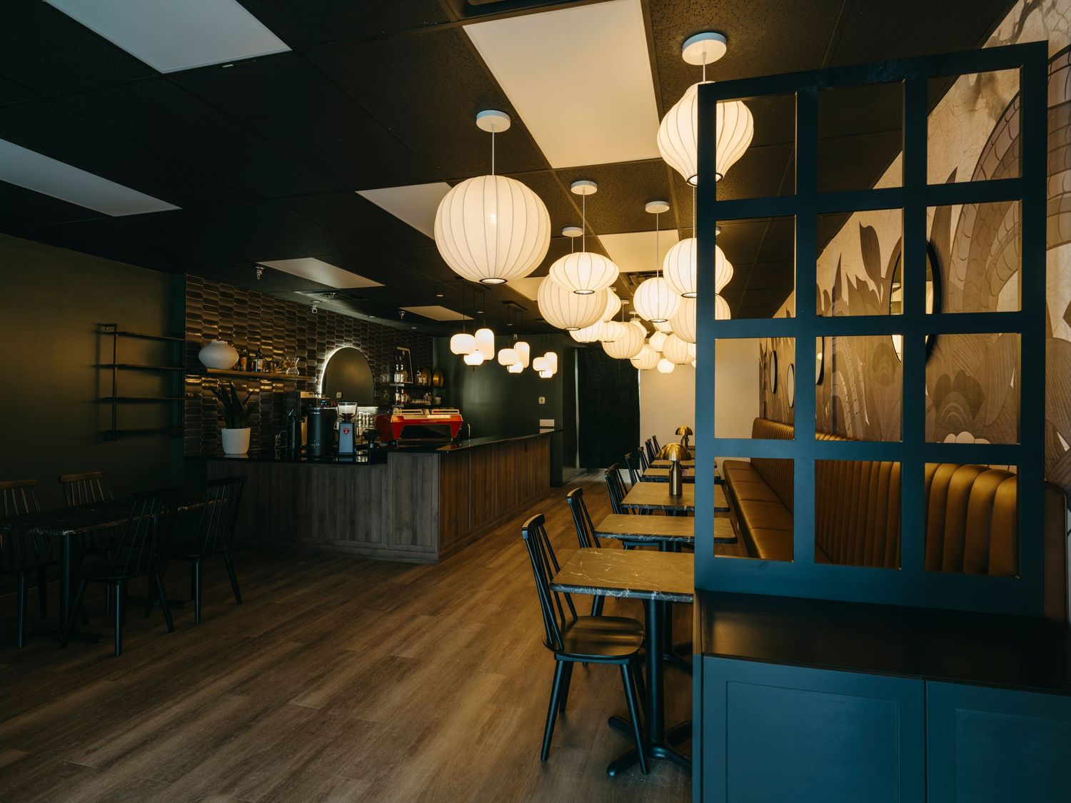 Modern restaurant interior with globe pendant lights, wooden tables, and blue partition dividers over hardwood floors.