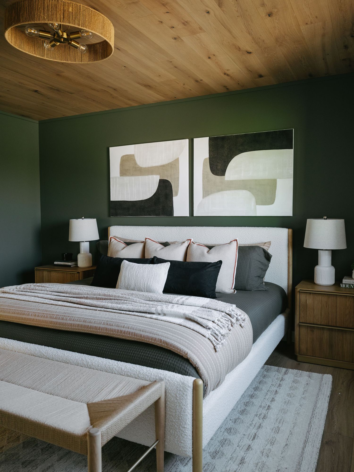 Green bedroom with wood ceiling, abstract art, upholstered bed, and rattan light fixture.