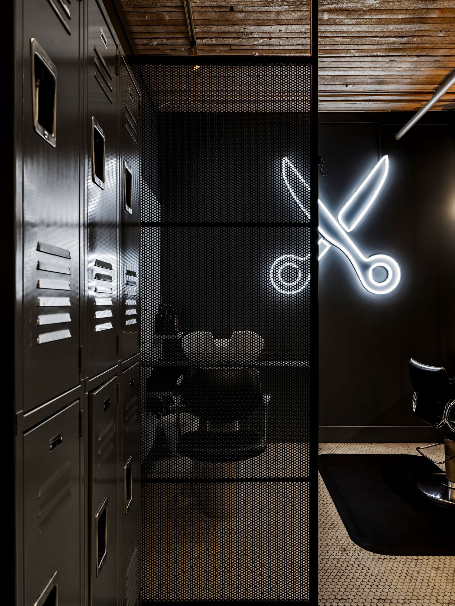 Black barbershop interior with neon scissors sign, mesh partition, and metal lockers.