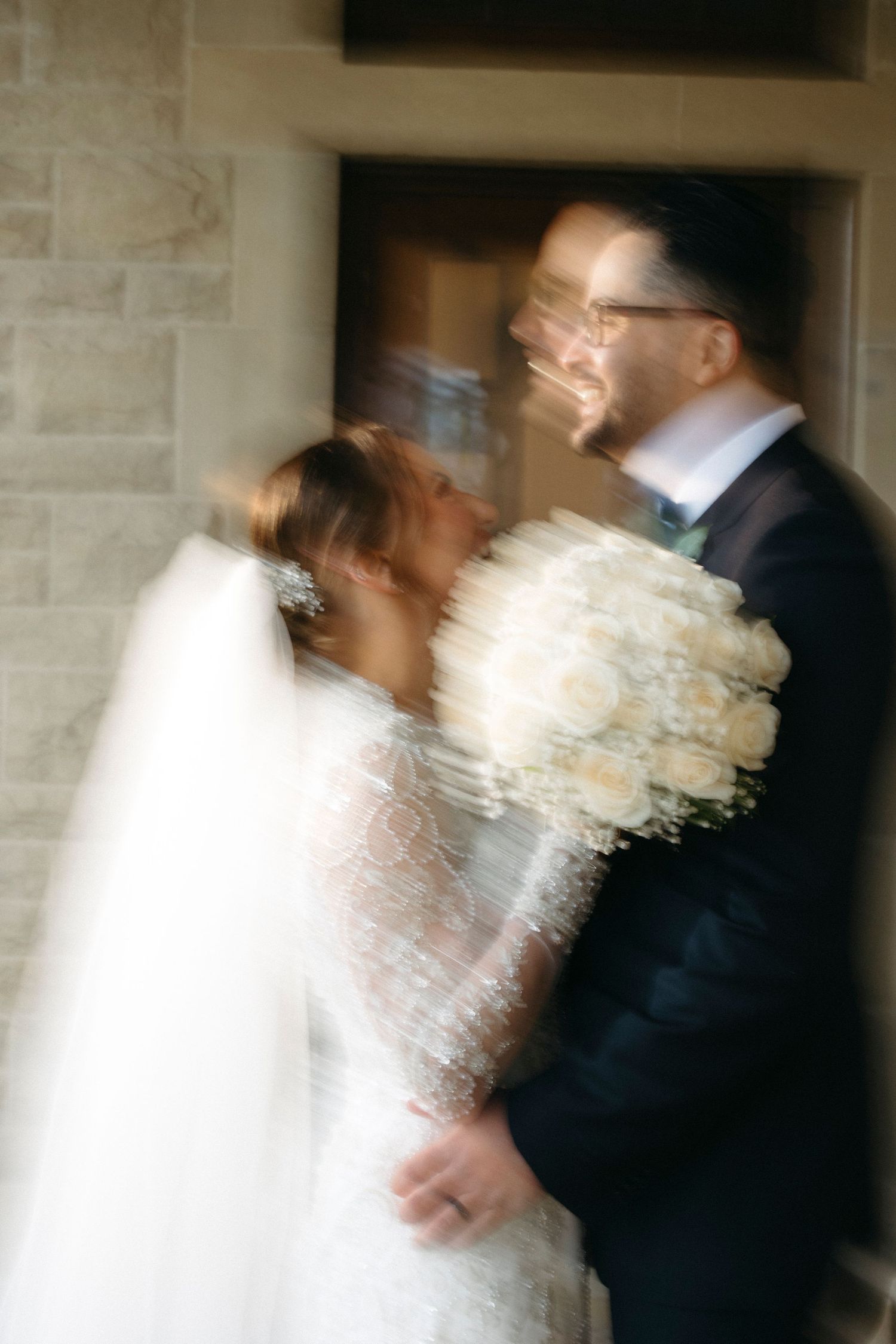 Artistic motion blur photo of bride and groom sharing intimate moment with white rose bouquet.
