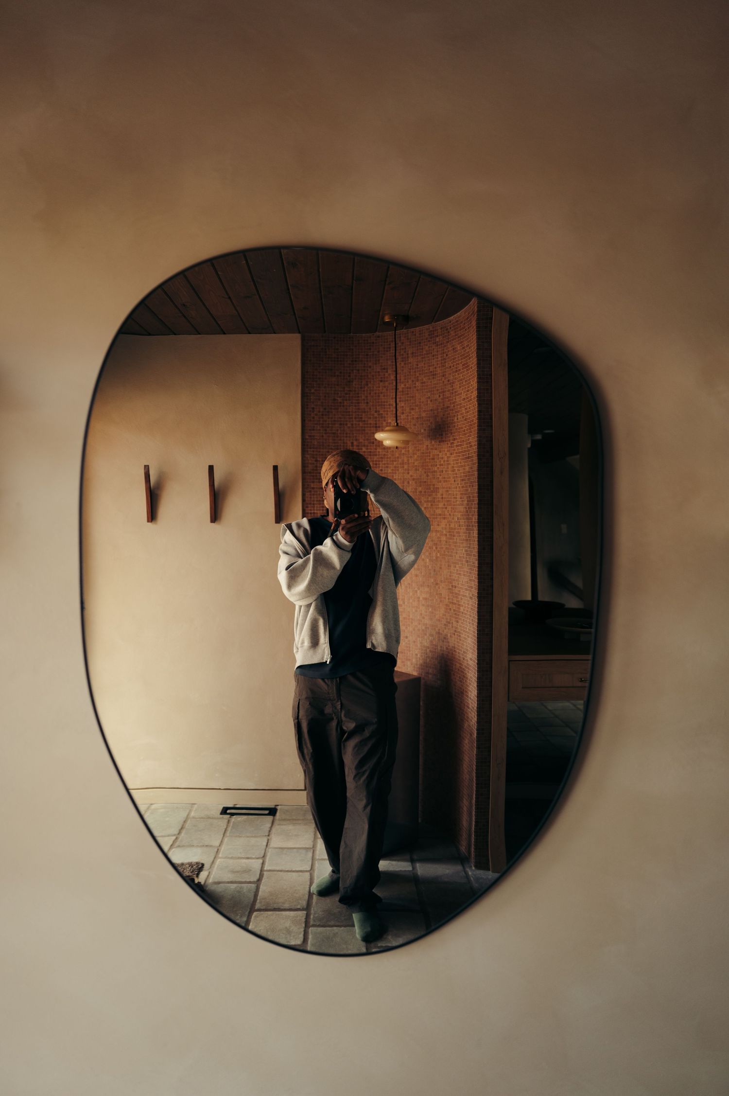 Person taking a mirror selfie in a stylish room with an asymmetric wall mirror and warm ambient lighting.