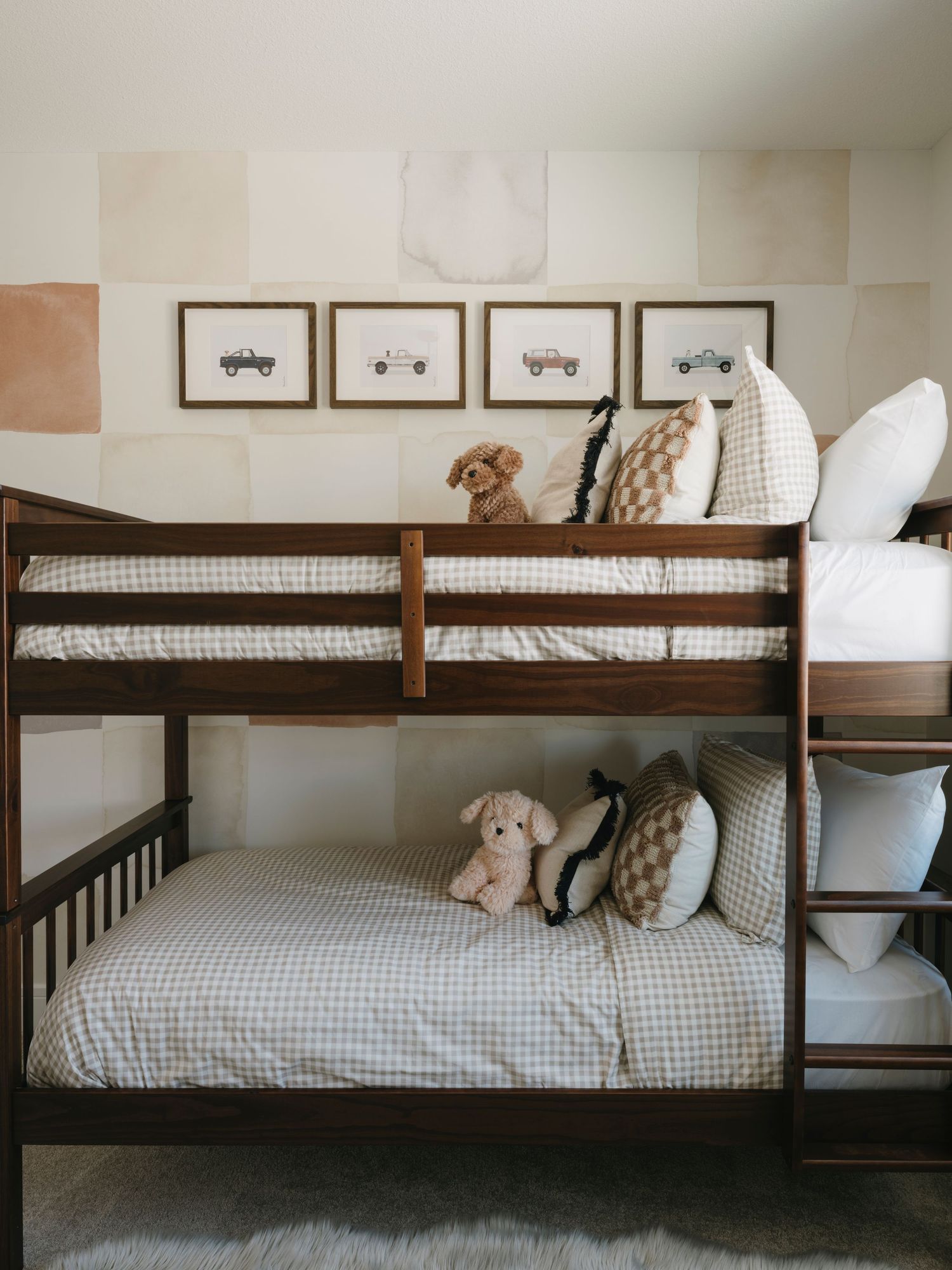 Dark walnut bunk beds with gingham bedding, stuffed animals, and framed vintage truck art on checkered wall.