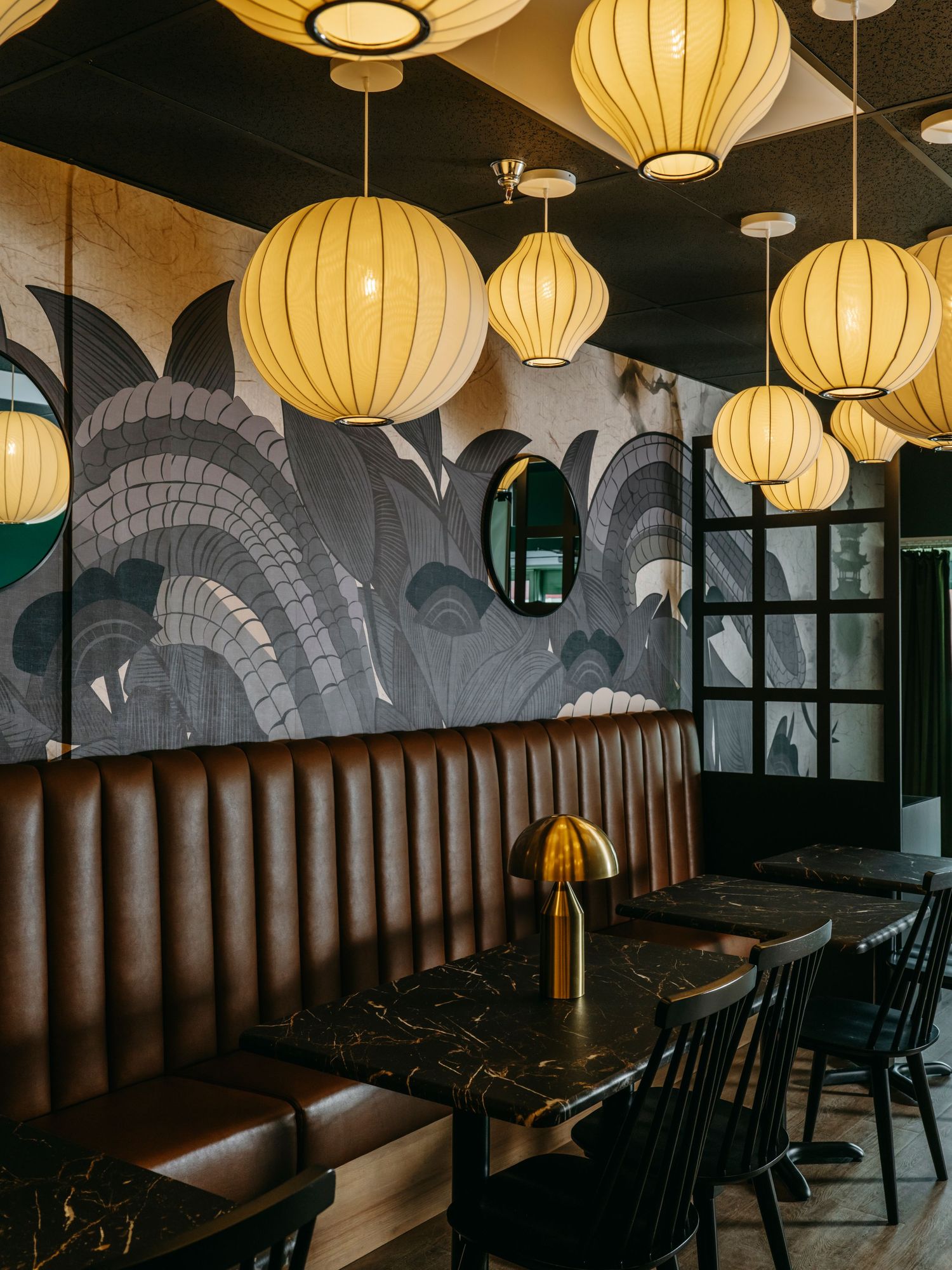 Cozy restaurant booth seating with brown leather banquettes, marble tables, and warm globe pendant lantern lights.