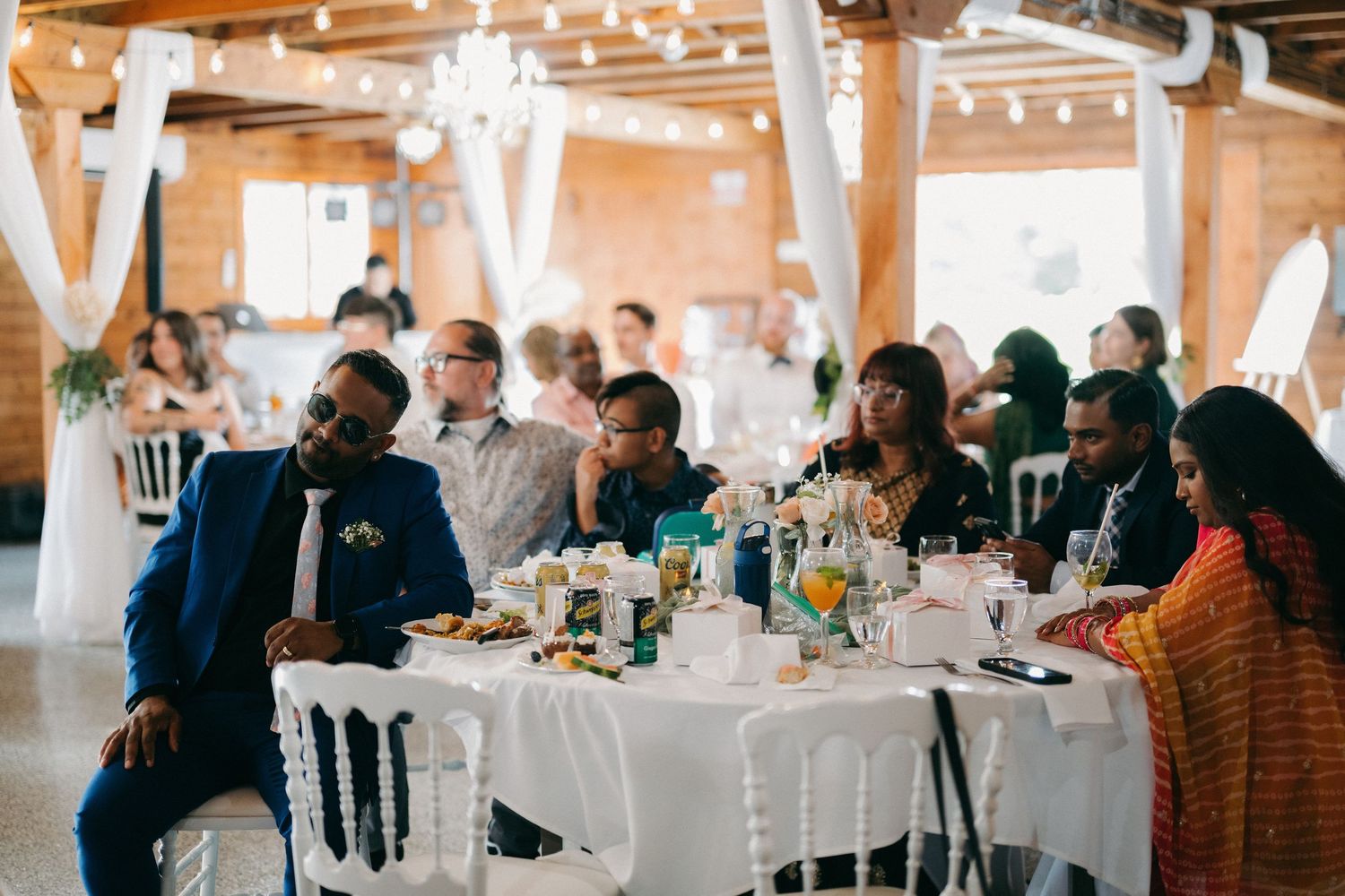 Wedding reception guests seated at round tables in rustic barn venue.