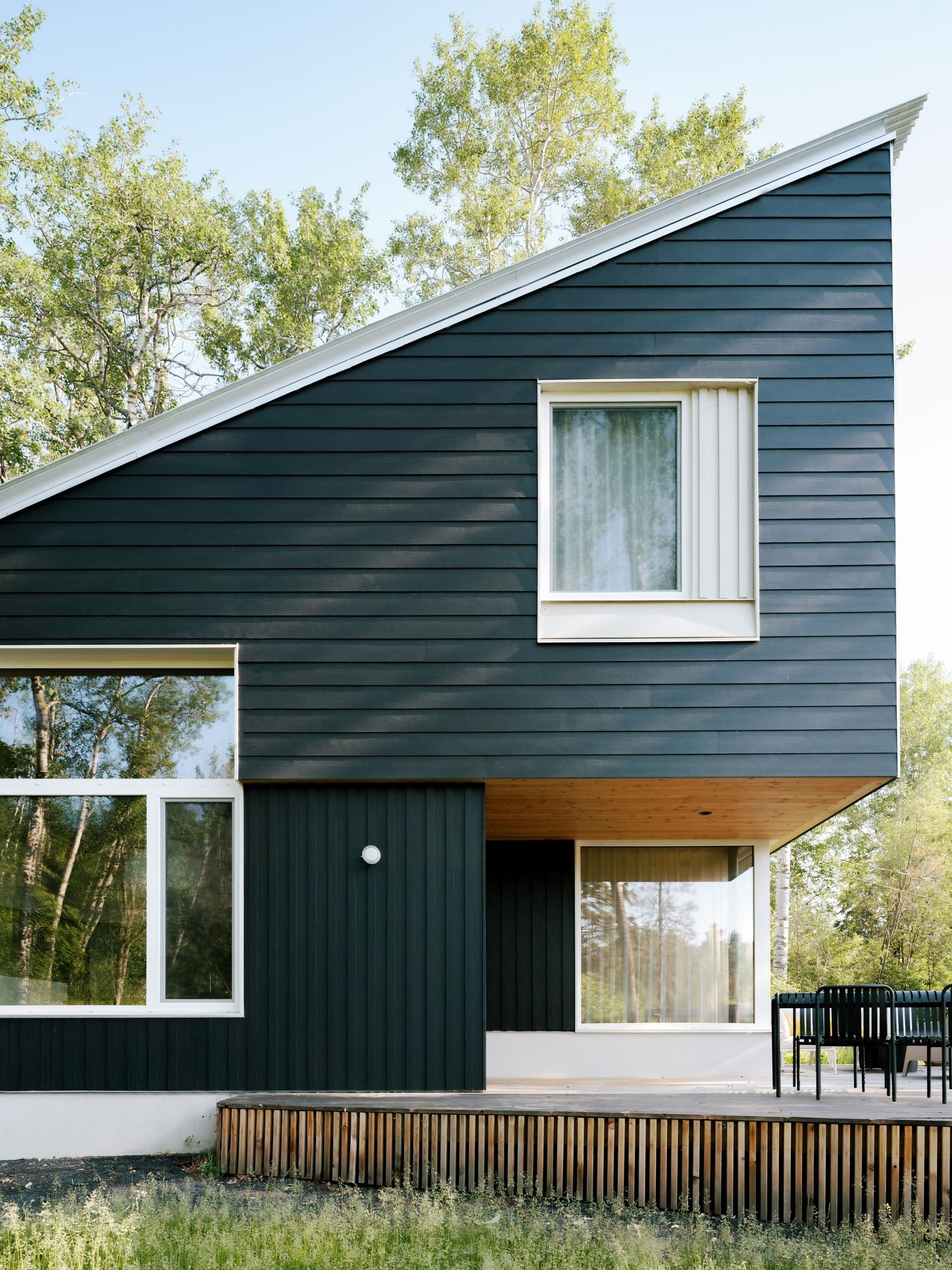Modern dark navy home exterior with asymmetric roofline, large windows, and wood deck surrounded by trees.