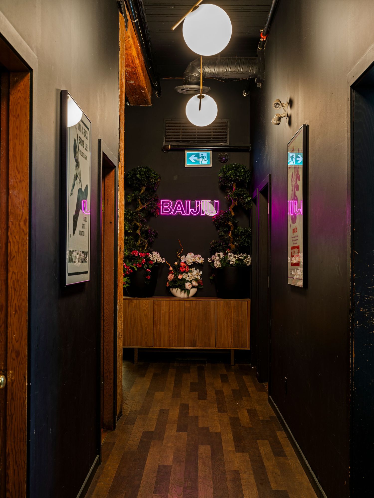 Dark hallway leading to Baijiu neon sign surrounded by floral arrangements and wood cabinetry.