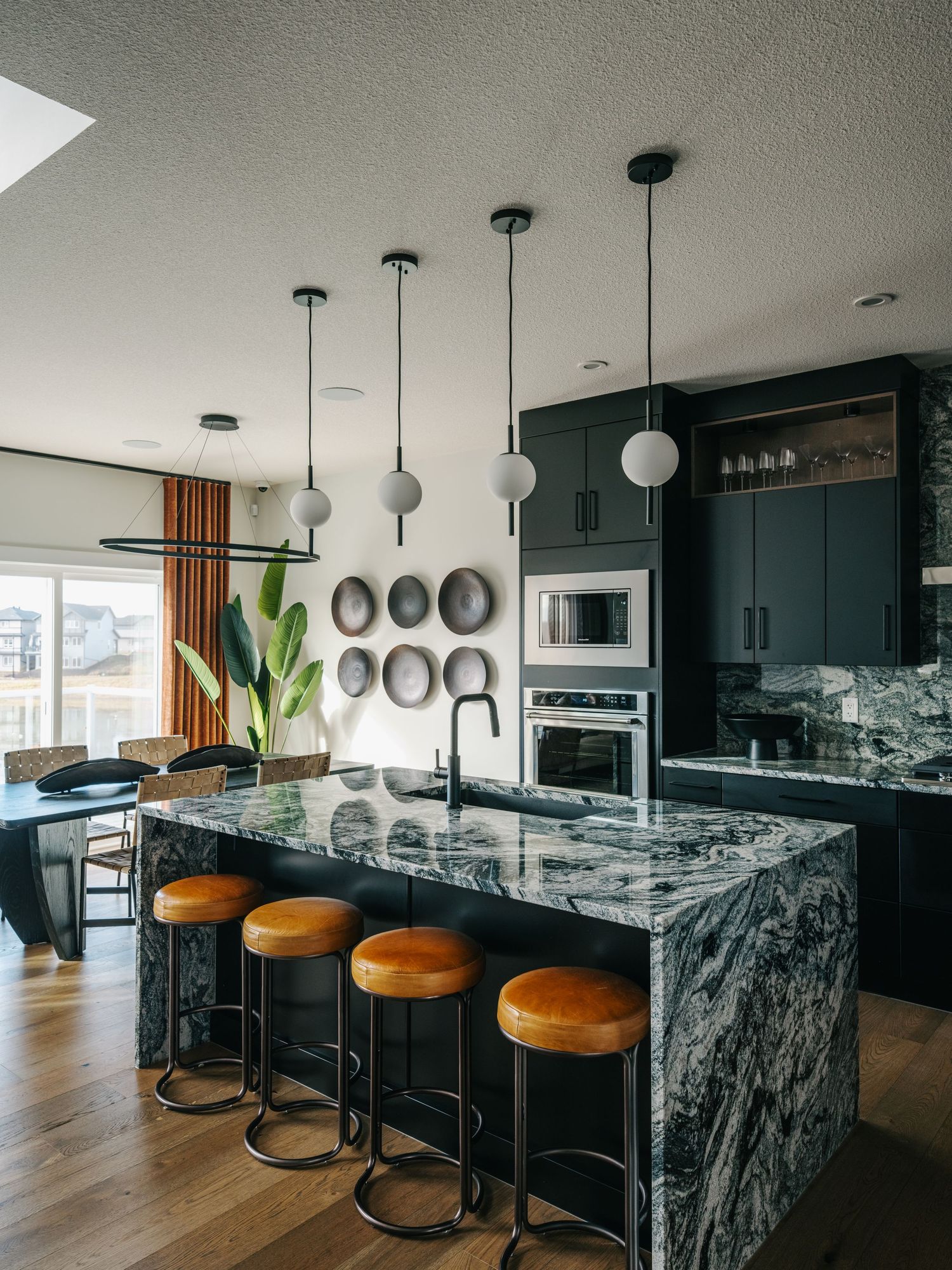 Modern kitchen with dark cabinets, green marble island, leather bar stools, pendant lights, and stainless steel appliances.