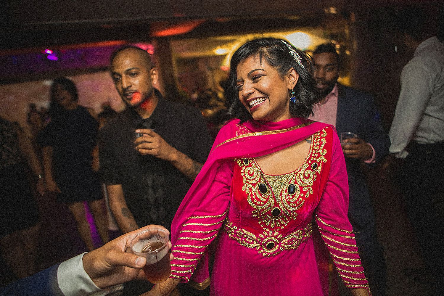 Woman in vibrant pink embroidered Indian lehenga dancing joyfully at a wedding reception party.