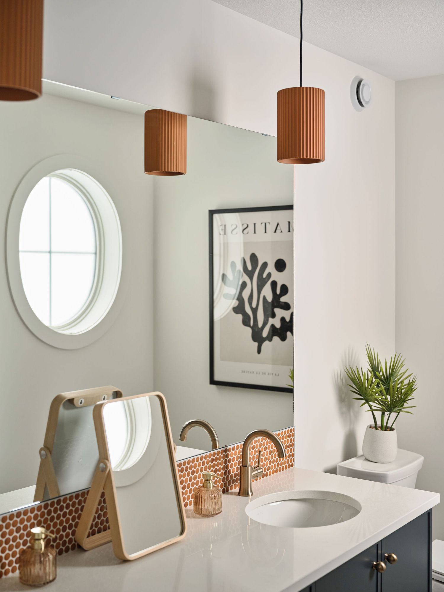 Modern bathroom vanity with terracotta pendant lights, oval porthole window, and copper hexagon tile backsplash.