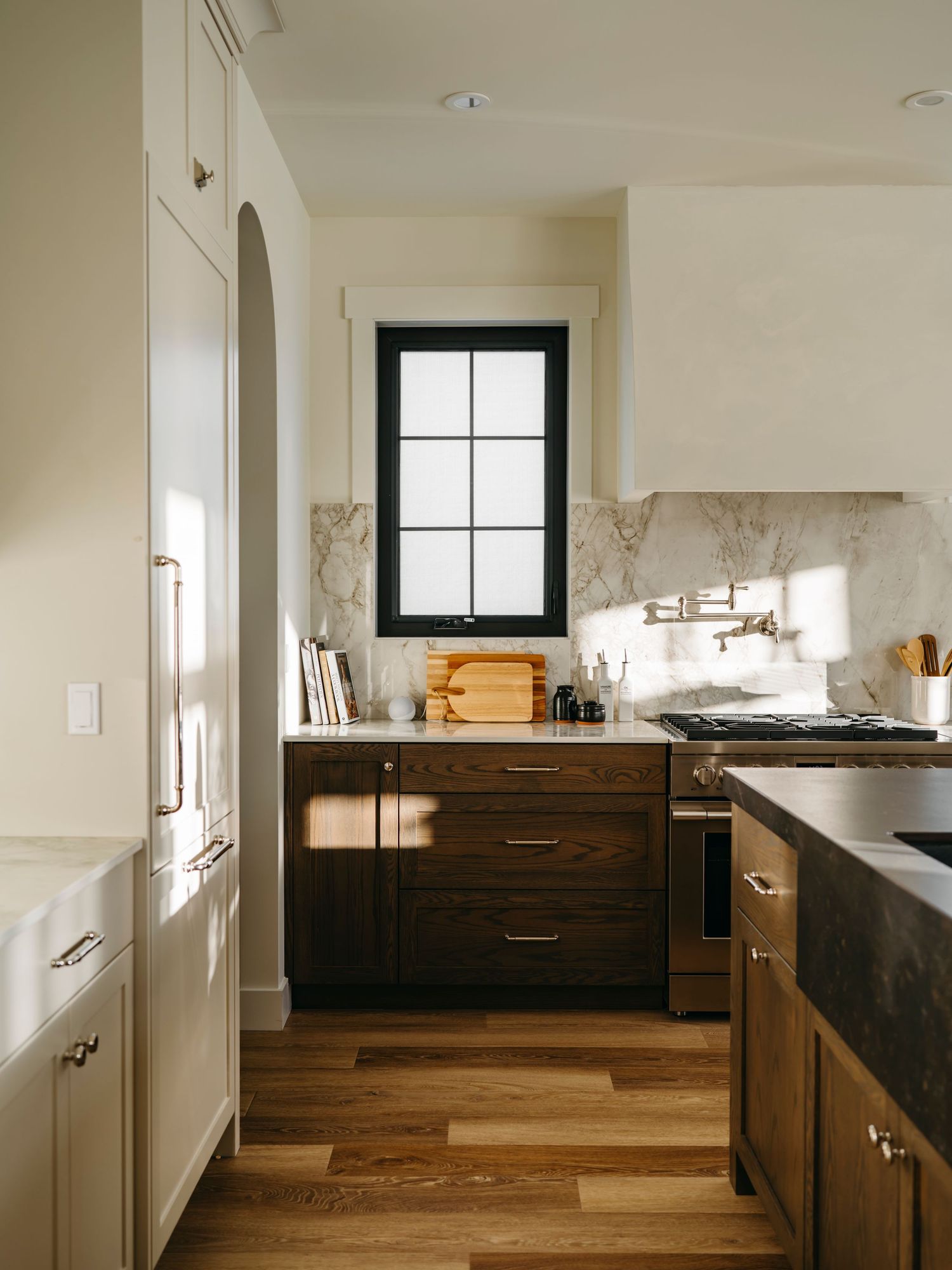 Elegant kitchen with dark wood cabinets, marble backsplash, brass hardware, white upper cabinets, and hardwood floors.