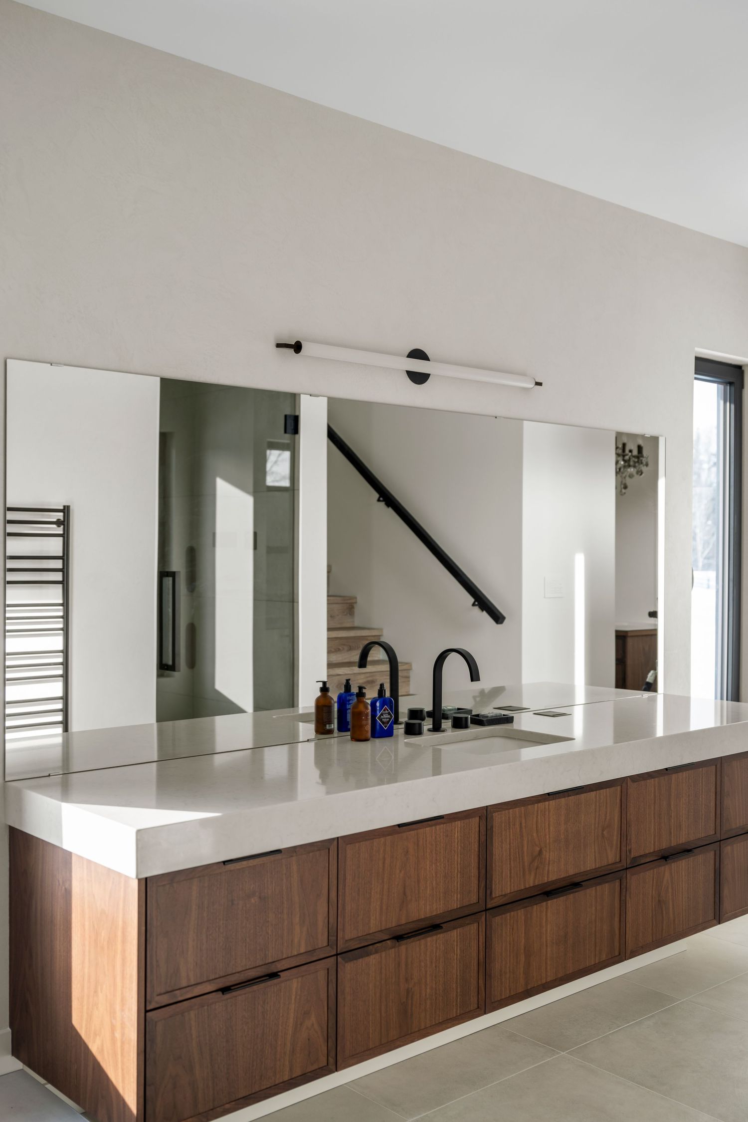 Minimalist bathroom vanity with walnut drawers, grey countertop, large mirror, and black matte faucet.