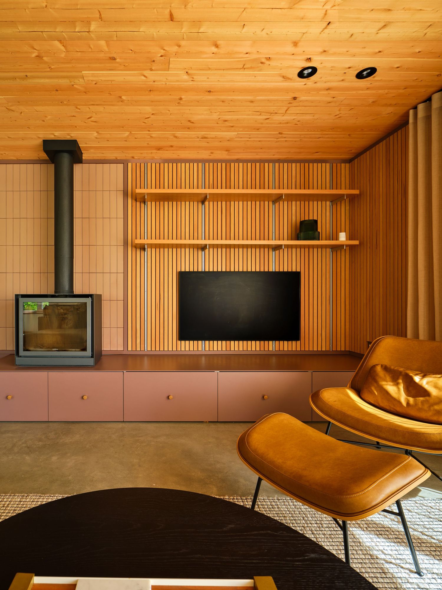 Cozy living room with wood slat TV wall, pink tile, freestanding fireplace, and leather lounge chair.