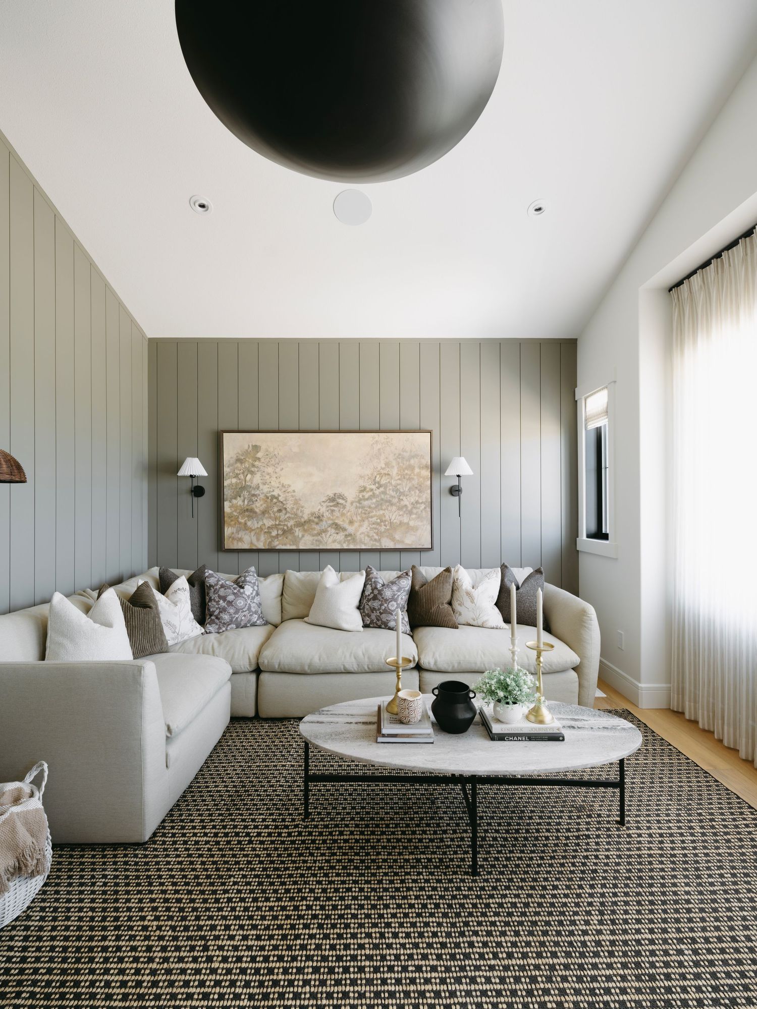 Cozy living room with sage green paneled walls, large sectional sofa, marble coffee table, and landscape artwork.