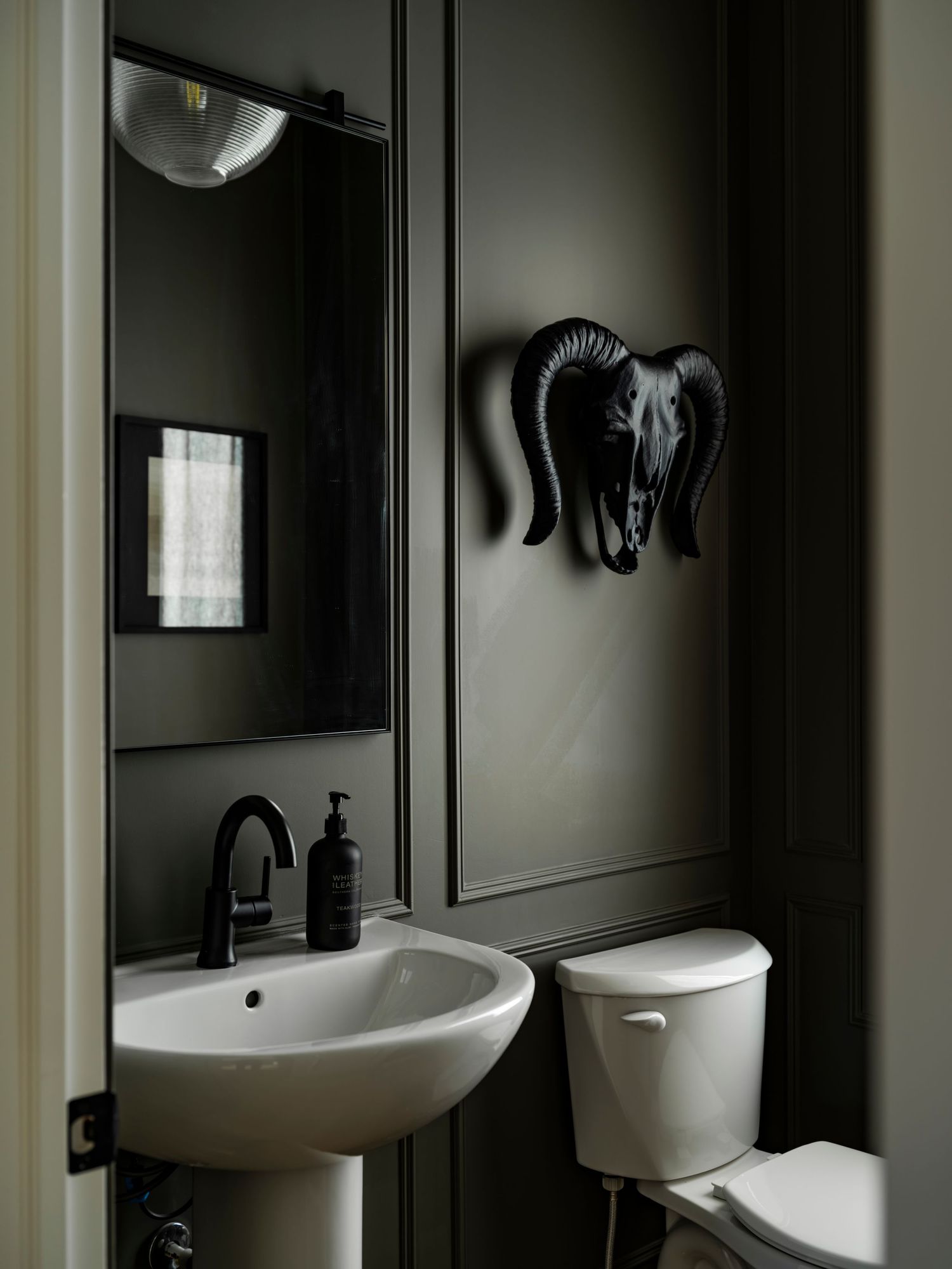 Edmonton interior photography by Ayo Erinle — dramatic dark olive powder room with pedestal sink and decorative wall art.