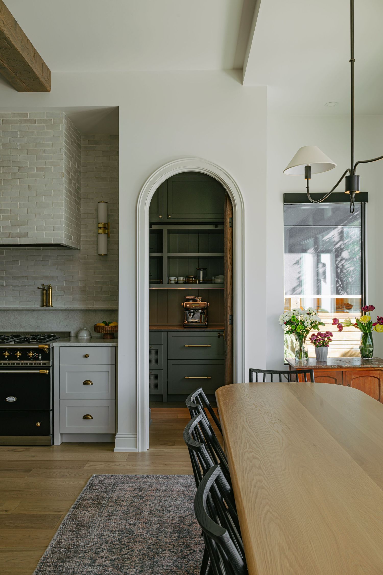 Modern kitchen with arched butler pantry entrance, black La Cornue range, subway tile backsplash, and wood dining table.
