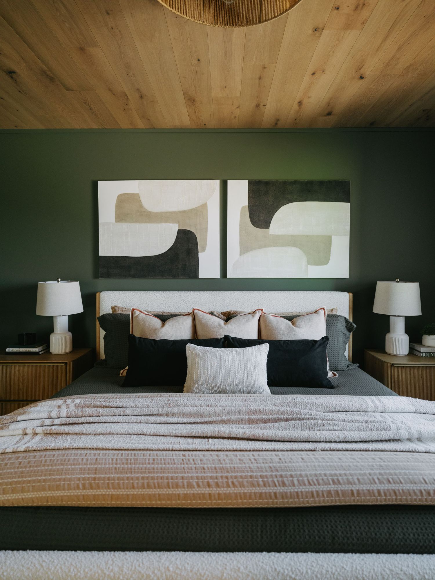 Cozy green bedroom with wood plank ceiling, abstract diptych art, and layered neutral bedding.