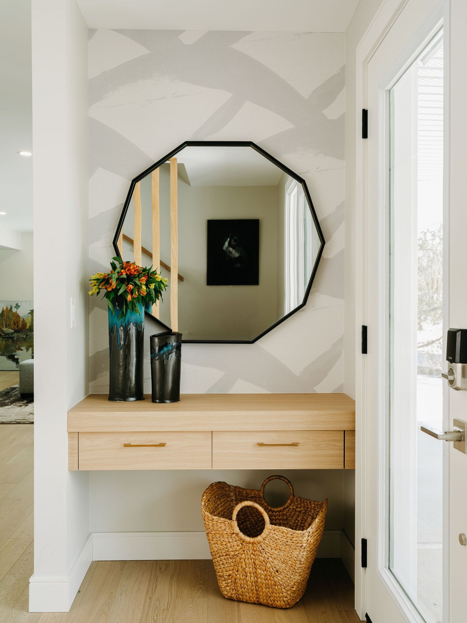 Entryway with geometric wallpaper, octagonal black mirror, floating light wood console table, and woven basket.