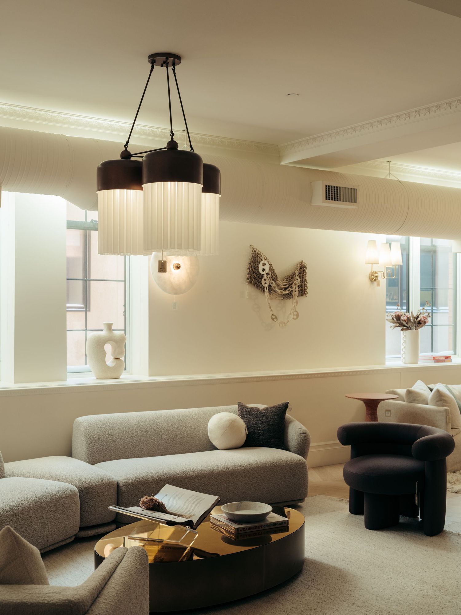 Elegant living room with pleated pendant light, grey modular sofa, brass coffee table, and cream walls with decorative sconces.
