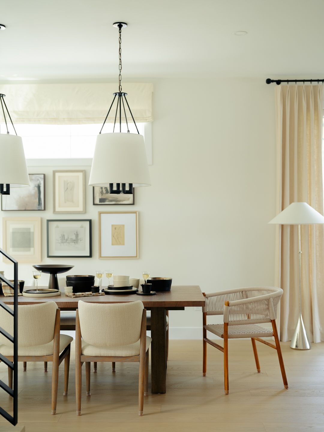 Neutral dining room with dark wood table, woven chairs, oversized pendant lights, and framed art gallery wall.