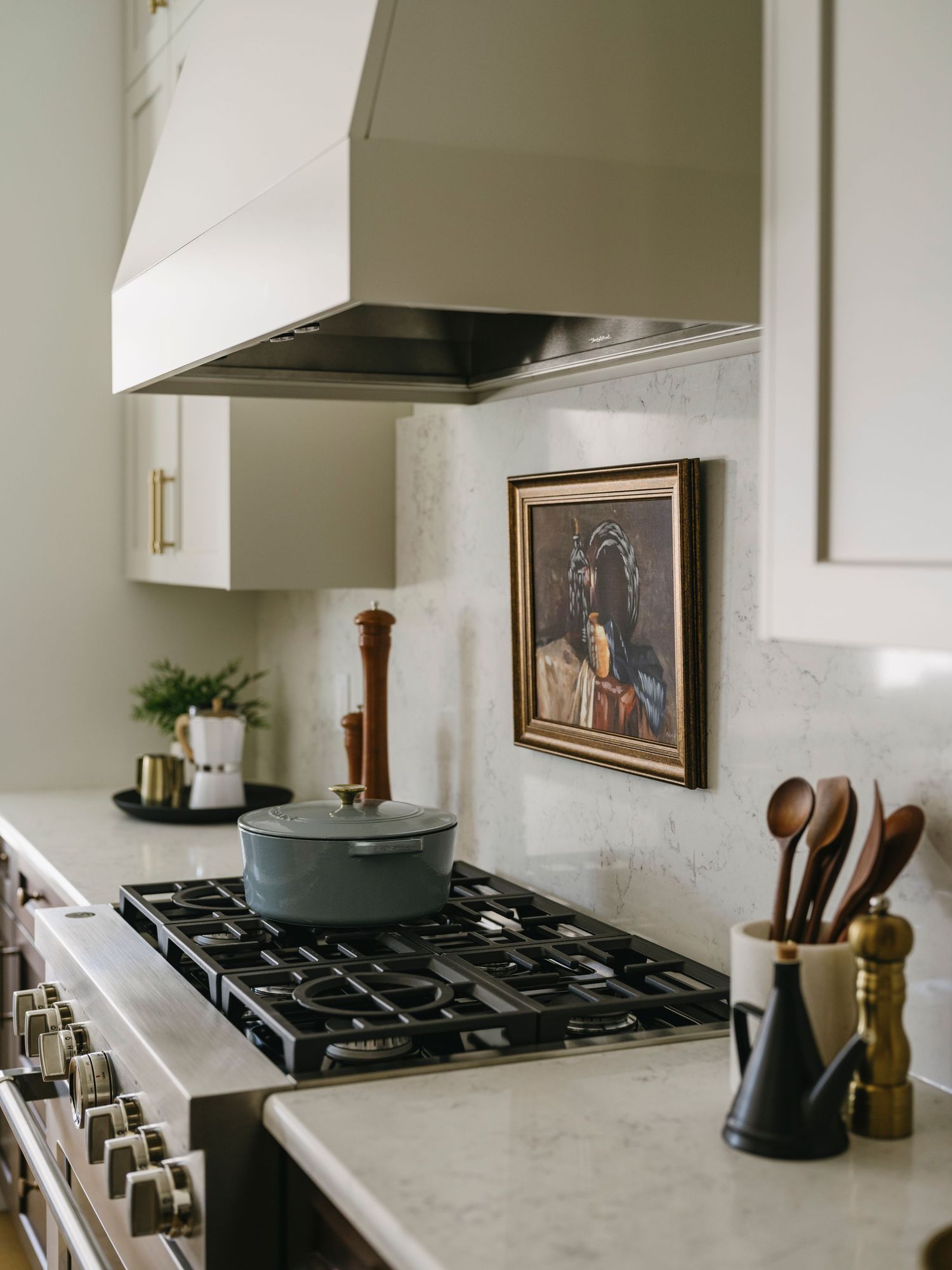 Elegant kitchen with marble backsplash, gas range, custom hood, and vintage portrait painting above stove.