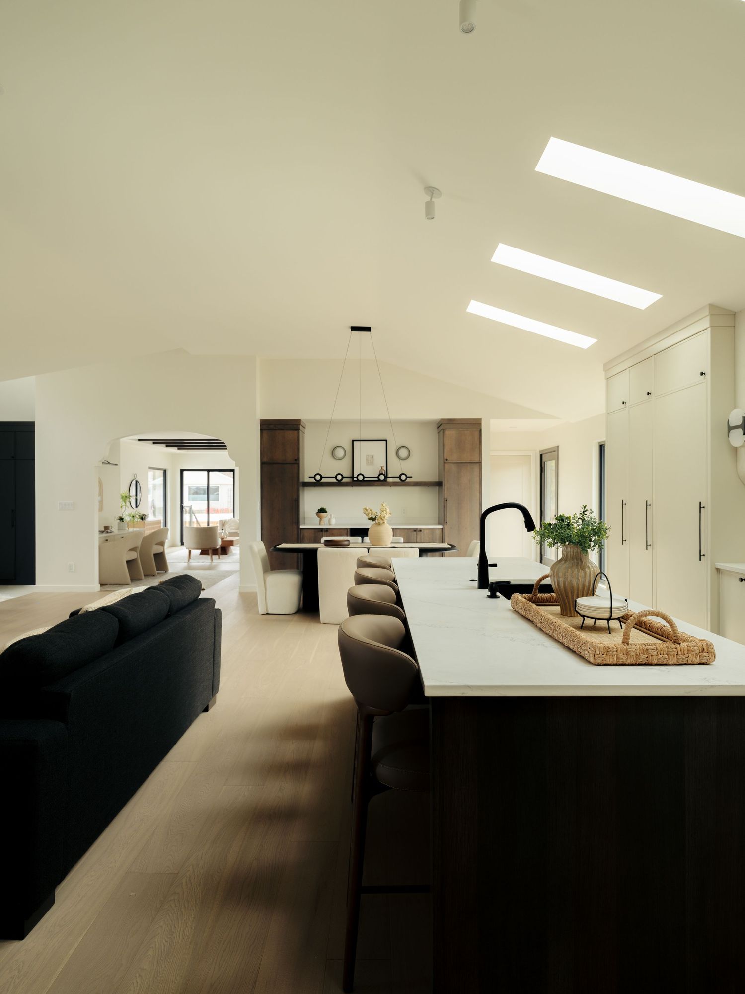 Open-plan kitchen and living area with vaulted ceiling, skylights, dark bar stools, white marble island, and warm wood tones.