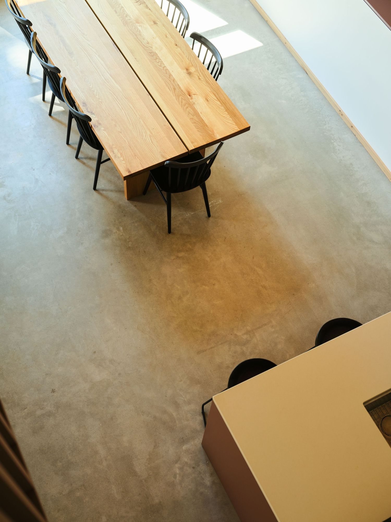 Aerial view of a long wood dining table with black chairs on polished concrete floor.