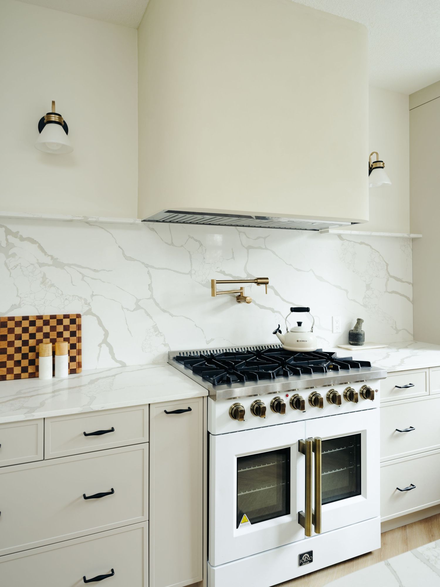 Elegant white kitchen with marble backsplash, white range with brass hardware, and globe wall sconces.