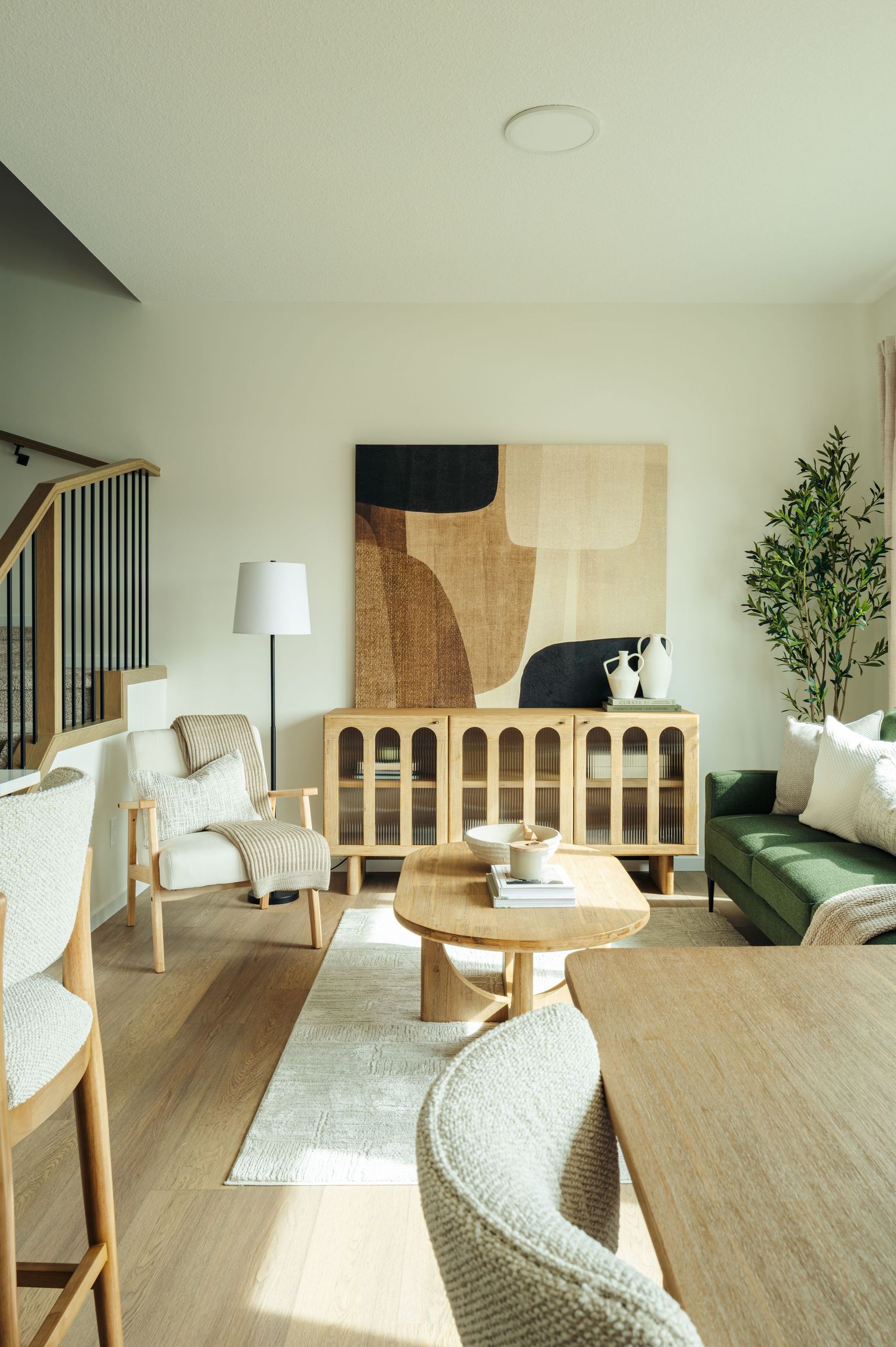 Modern living room with green sofa, wooden sideboard, abstract wall art, round coffee table, and neutral tones on light hardwood floors.