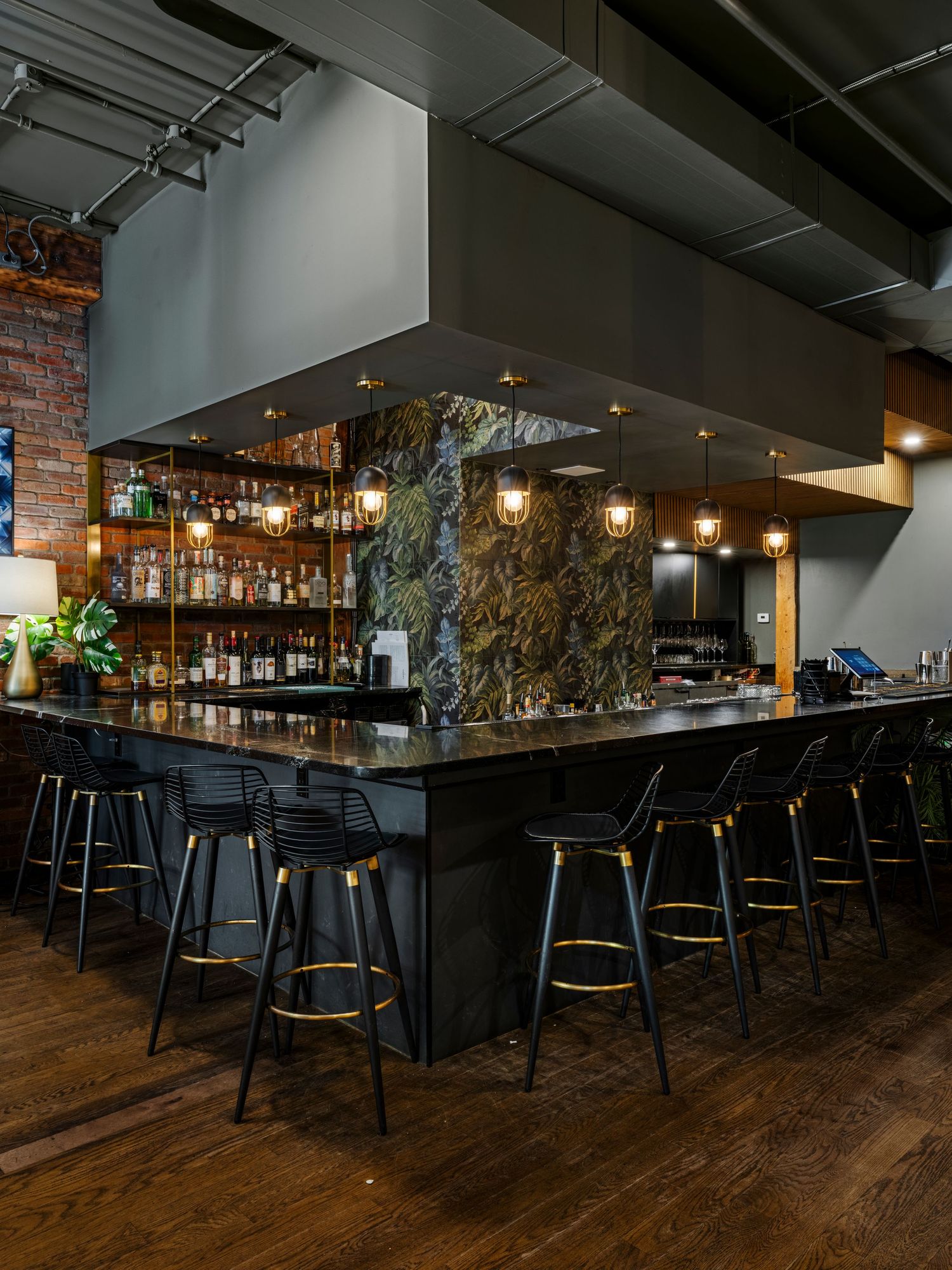 Upscale bar interior with black counter, bar stools, marble backsplash, and backlit liquor shelves.