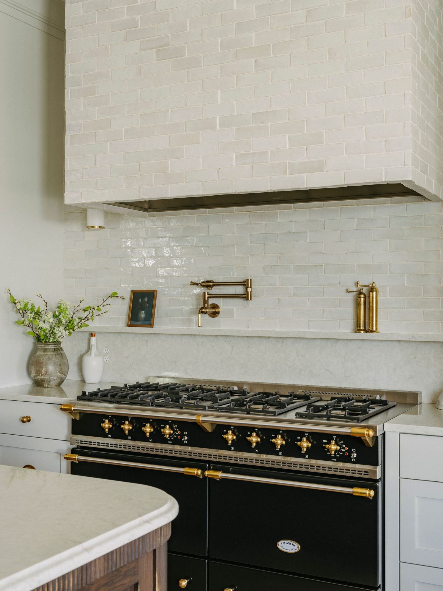 Luxury kitchen featuring black La Cornue range with gold accents, brass pot filler, and white zellige tile backsplash.