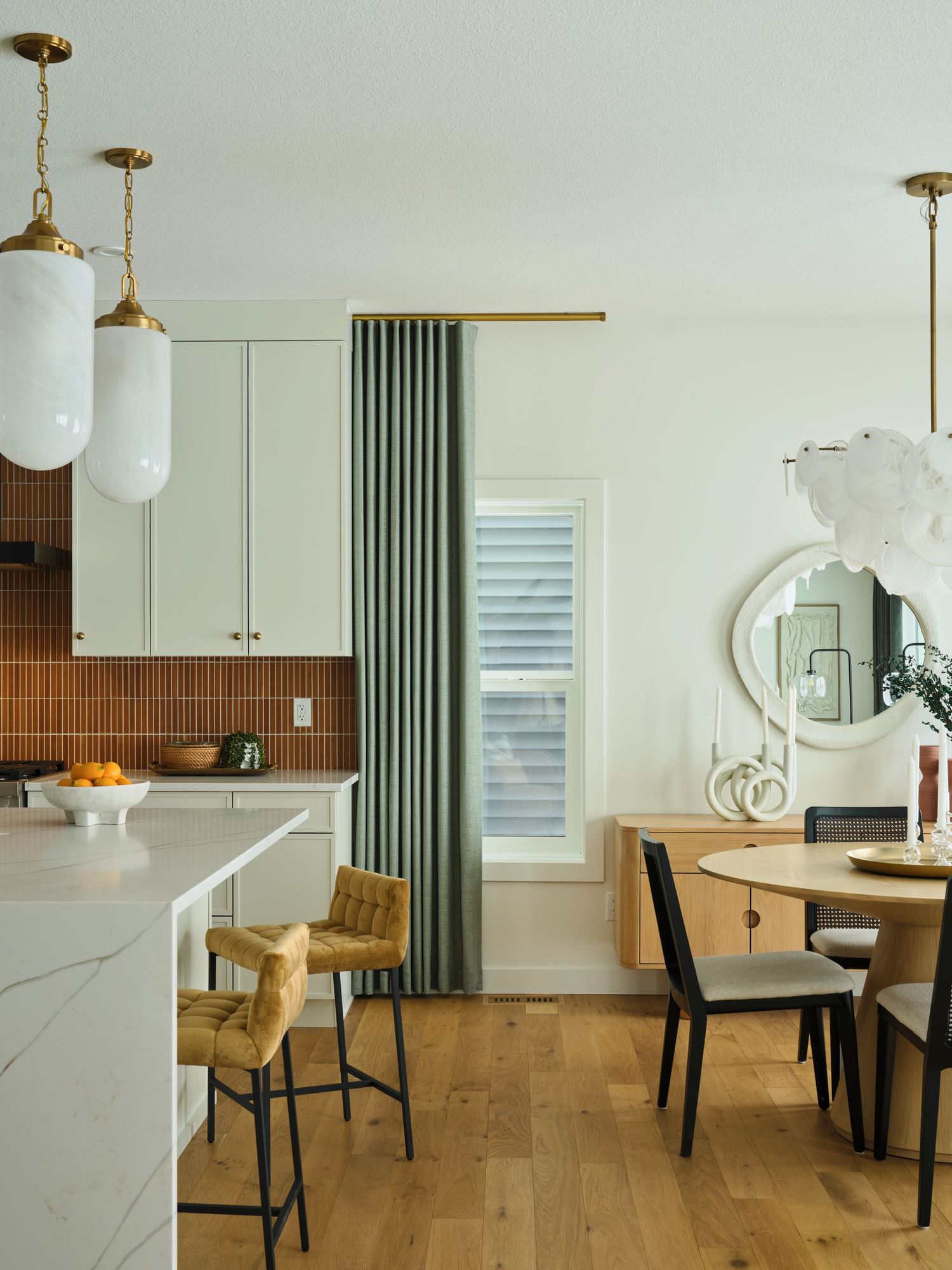 Kitchen and dining area with terracotta backsplash, marble island, green curtains, and brass pendant lights.