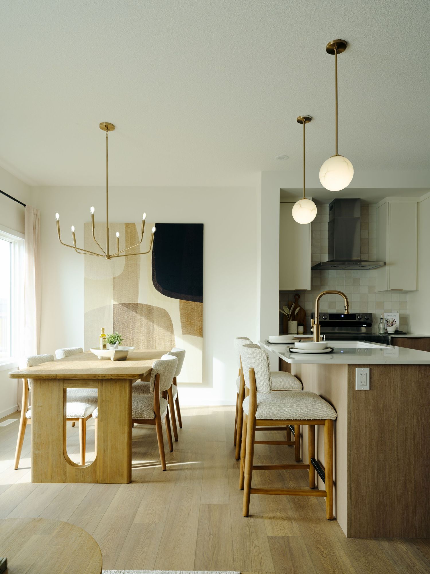 Modern open-plan dining and kitchen with light wood furniture, brass pendant lights, and neutral tones.