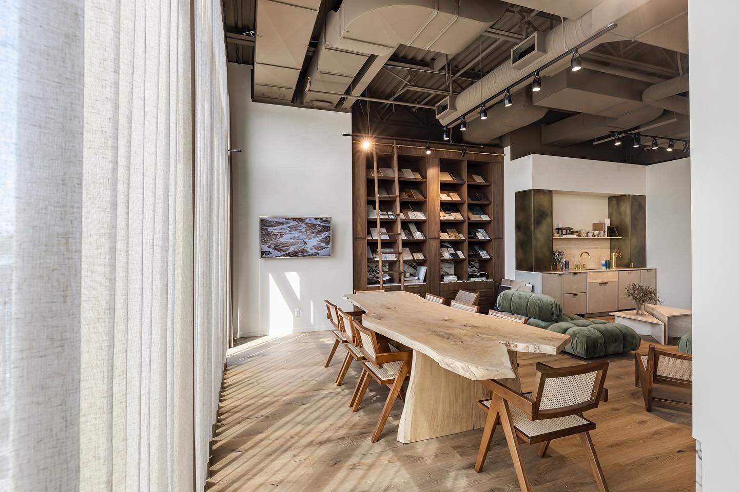 Modern open-plan dining area with live-edge wood table, designer chairs, built-in shelving, and industrial exposed ceiling details.