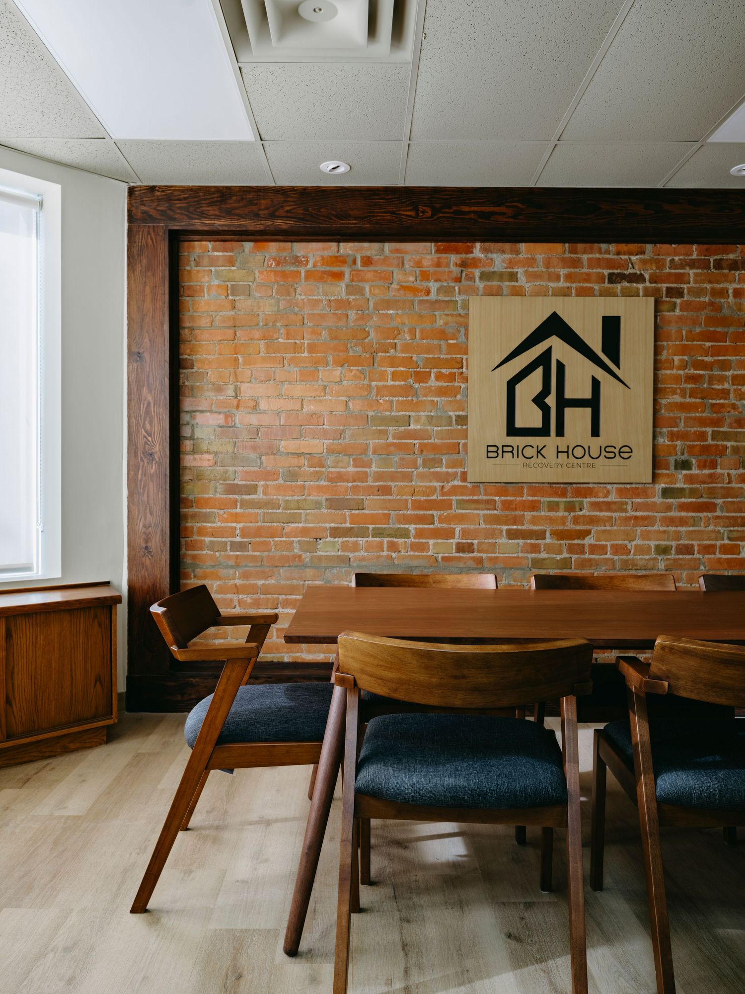 Modern conference room with exposed brick wall, wood dining table, and Brick House logo sign.